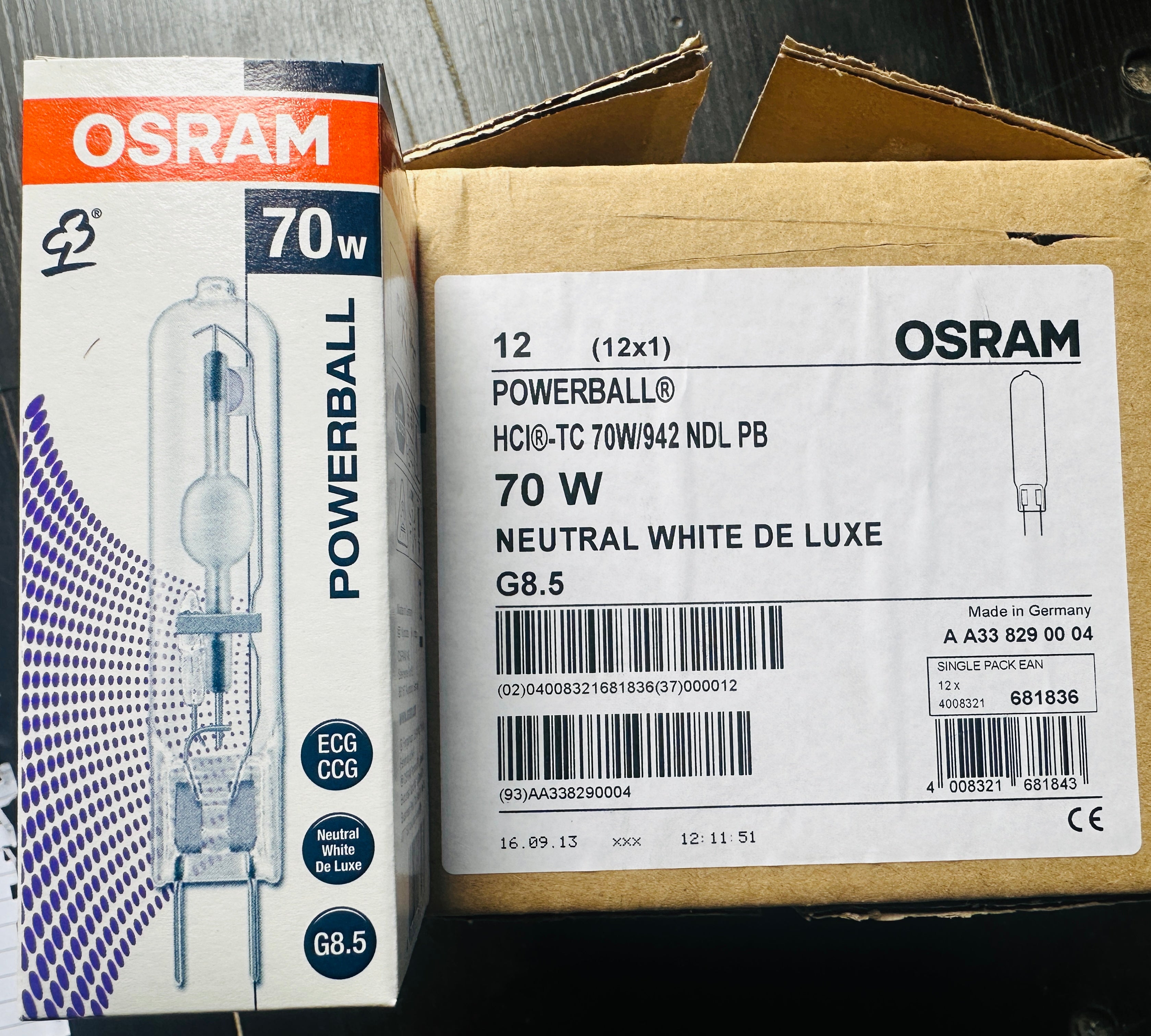 Two OSRAM POWERBALL 70W neutral white light bulbs in their original retail packaging, shown side-by-side on a dark wooden surface.